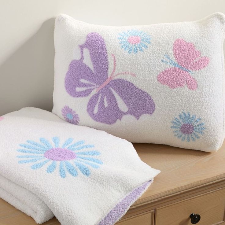 two white pillows sitting on top of a wooden dresser next to a pillow with butterflies