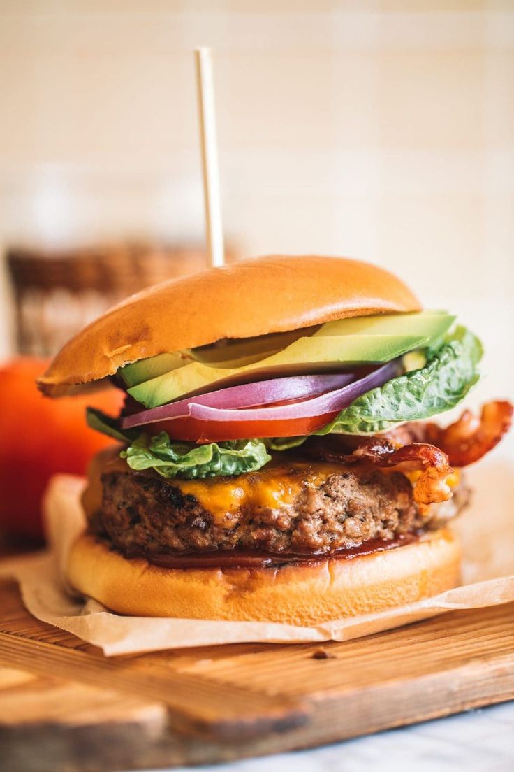 a cheeseburger with bacon, lettuce and tomato on a cutting board