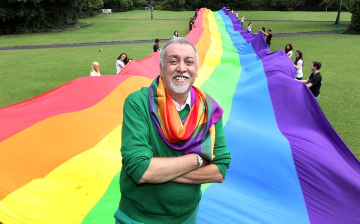 an old man standing in front of a rainbow colored kite that says gay lagi? dau hieu nahn biet gay