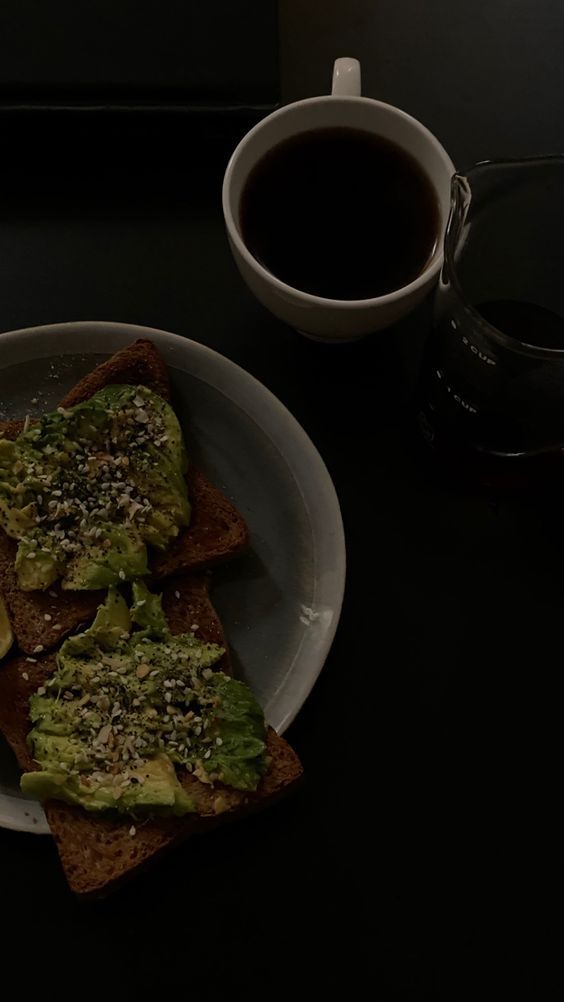 two pieces of toast with avocado on them next to a cup of coffee