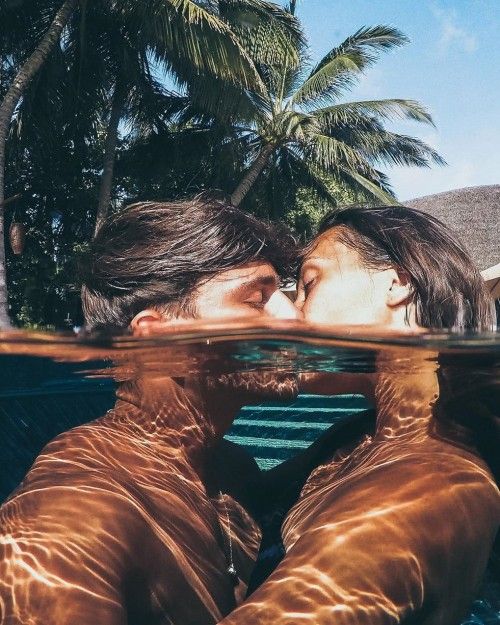 two people are kissing under the water in front of palm trees