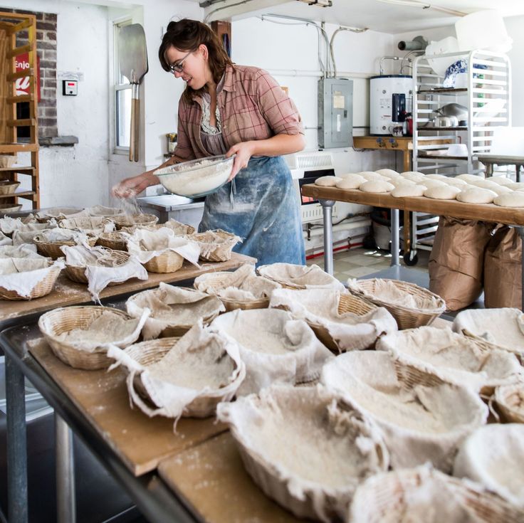 a woman is making bread in a kitchen with lots of muffins on the counter