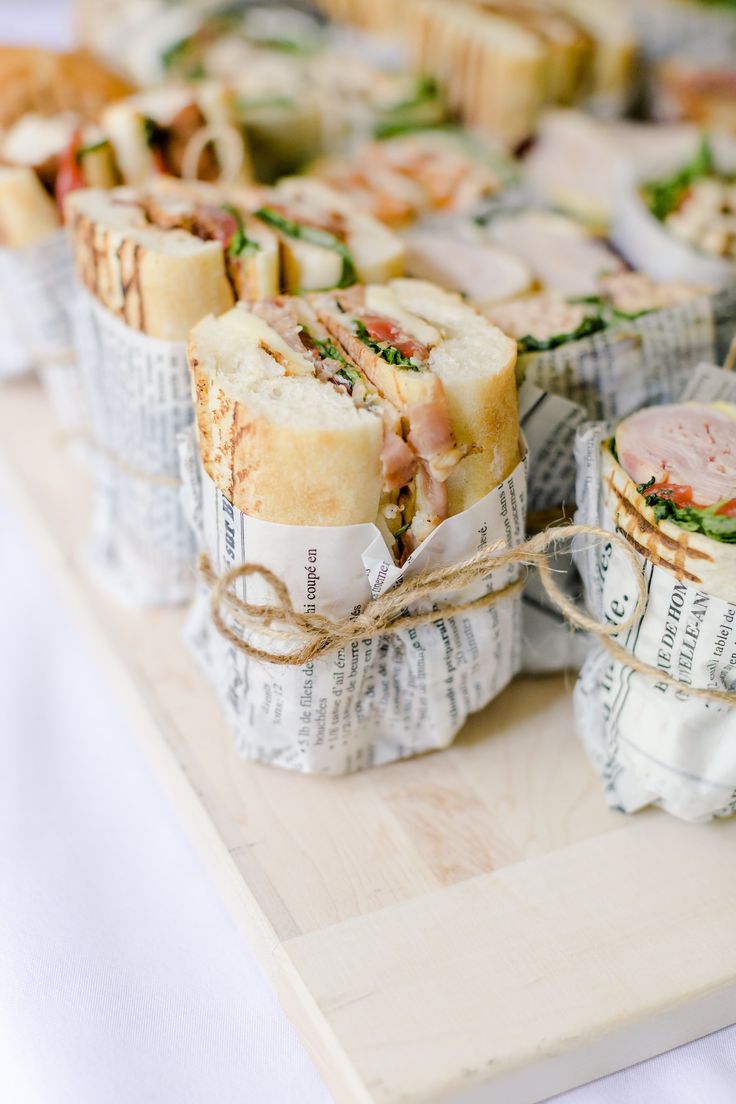 sandwiches wrapped in newspaper sitting on top of a wooden cutting board next to each other