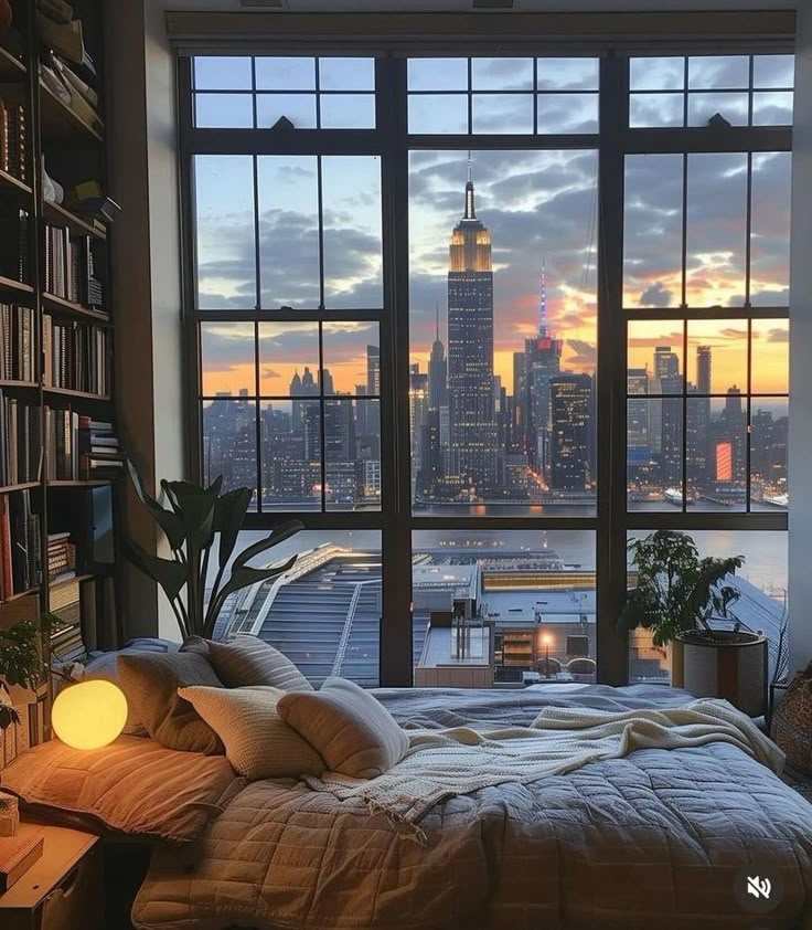 a bedroom with a large window and a view of the city at sunset or dawn