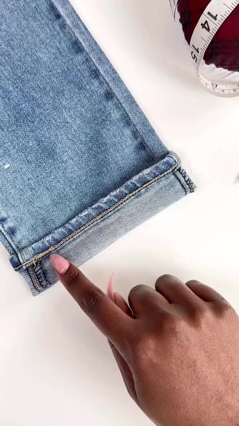 a person's hand pointing at a pair of jeans with a measuring tape next to it