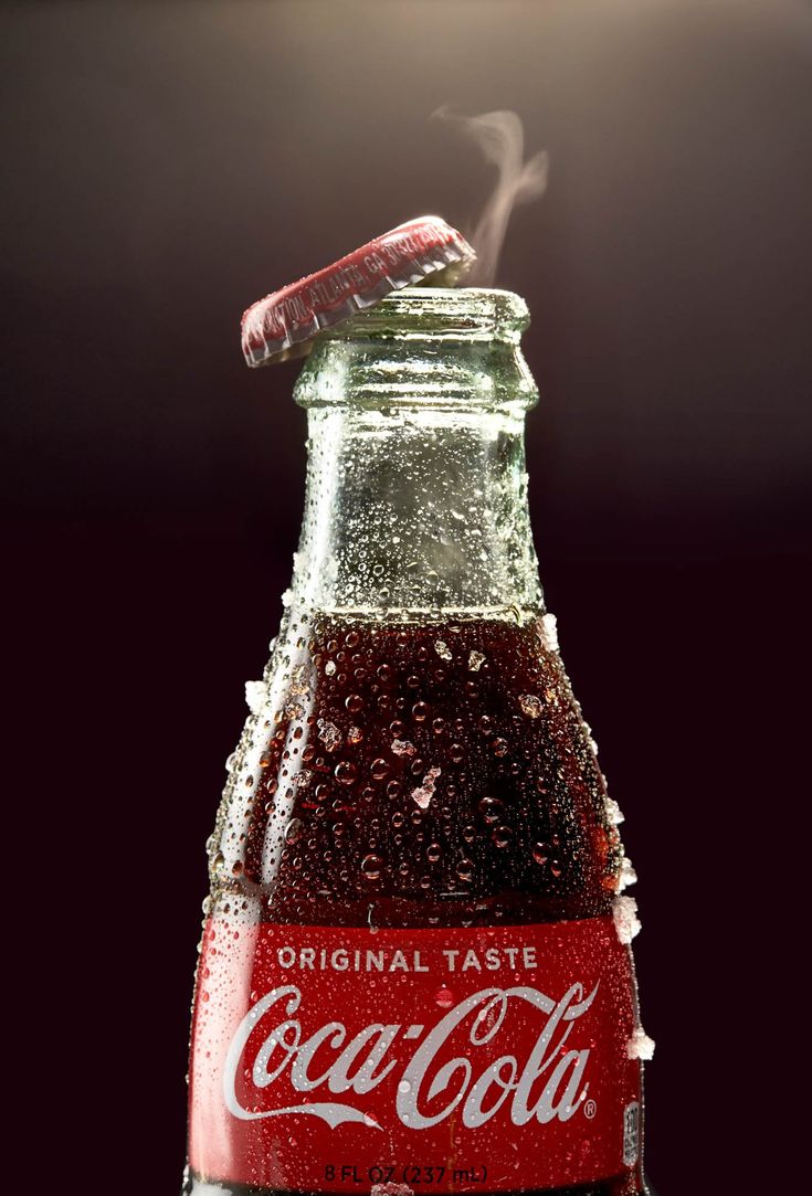 a coca - cola bottle with steam coming out of the top, on a dark background