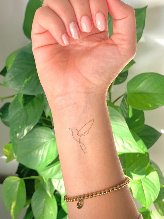 a woman's arm with a small bird tattoo on the wrist and a gold chain bracelet