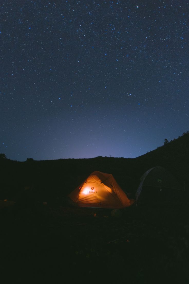 a tent is lit up at night with the stars in the sky above and below