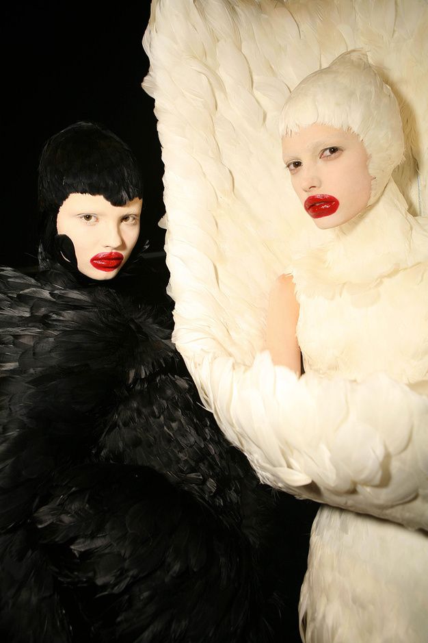 two women dressed in black and white with large feathers on their shoulders, both wearing red lipstick