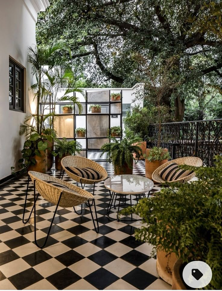 an outdoor patio with wicker furniture and potted plants on the side wall, black and white checkered tile flooring