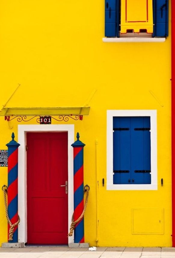 a red door and blue shutters on a yellow building