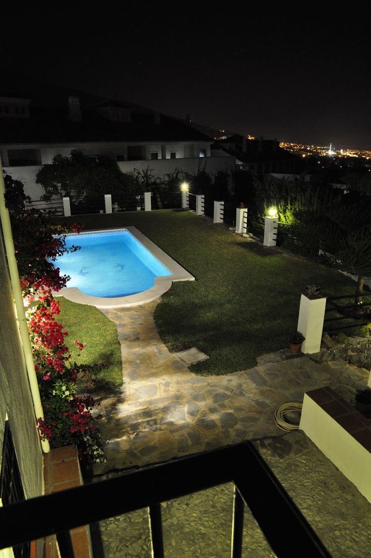 an aerial view of a pool at night with lights shining on the grass and trees