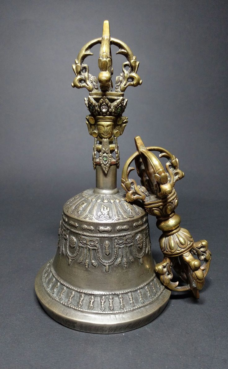 an antique bell with two figurines on the top and one sitting on it's side