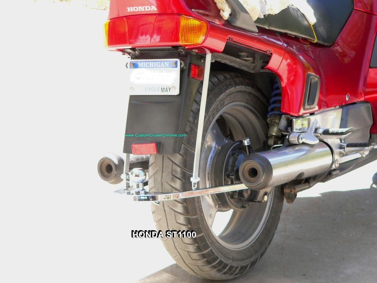 the rear end of a red motorcycle parked in front of a white building with a black cat sitting on it's back tire