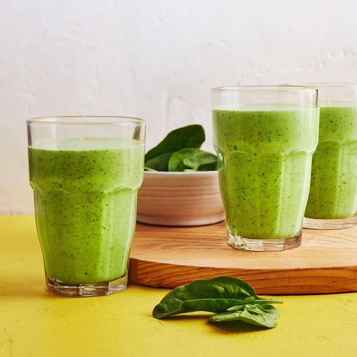 three glasses filled with green smoothie sitting on top of a table