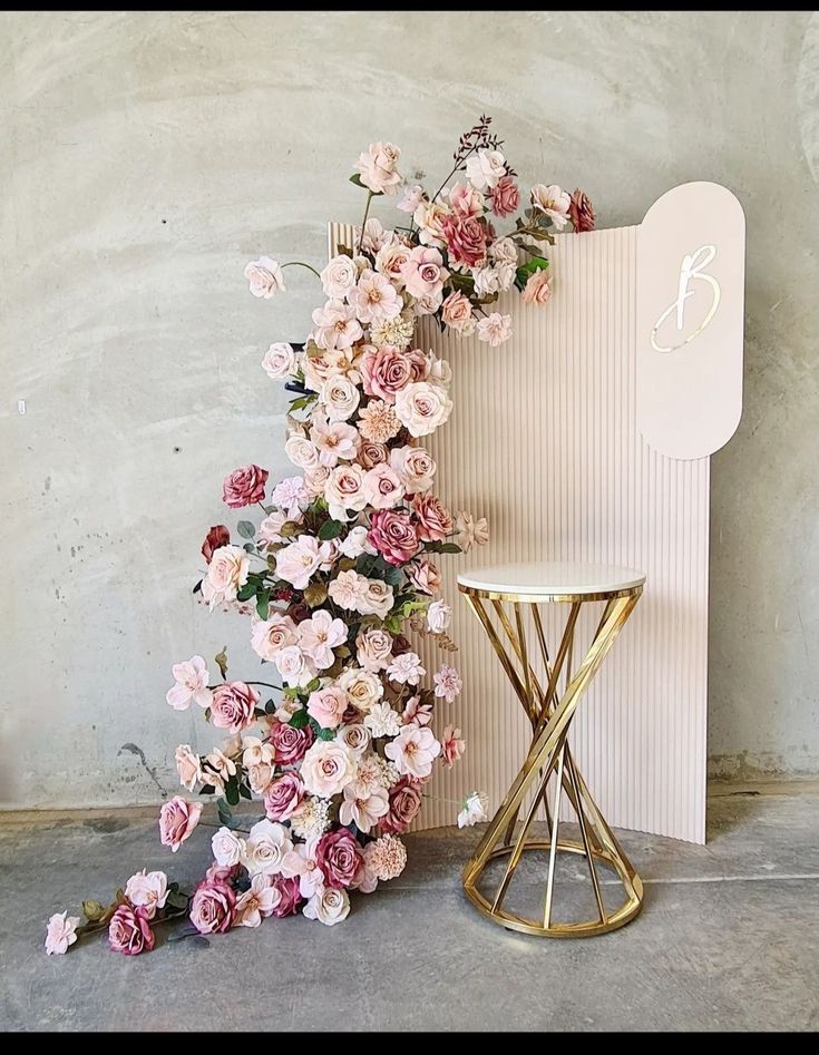 pink flowers are growing on the side of a wall next to a stool and table