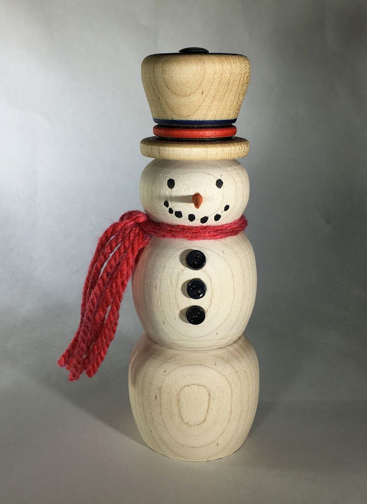 a wooden snowman with a red scarf and hat on it's head, standing in front of a white background