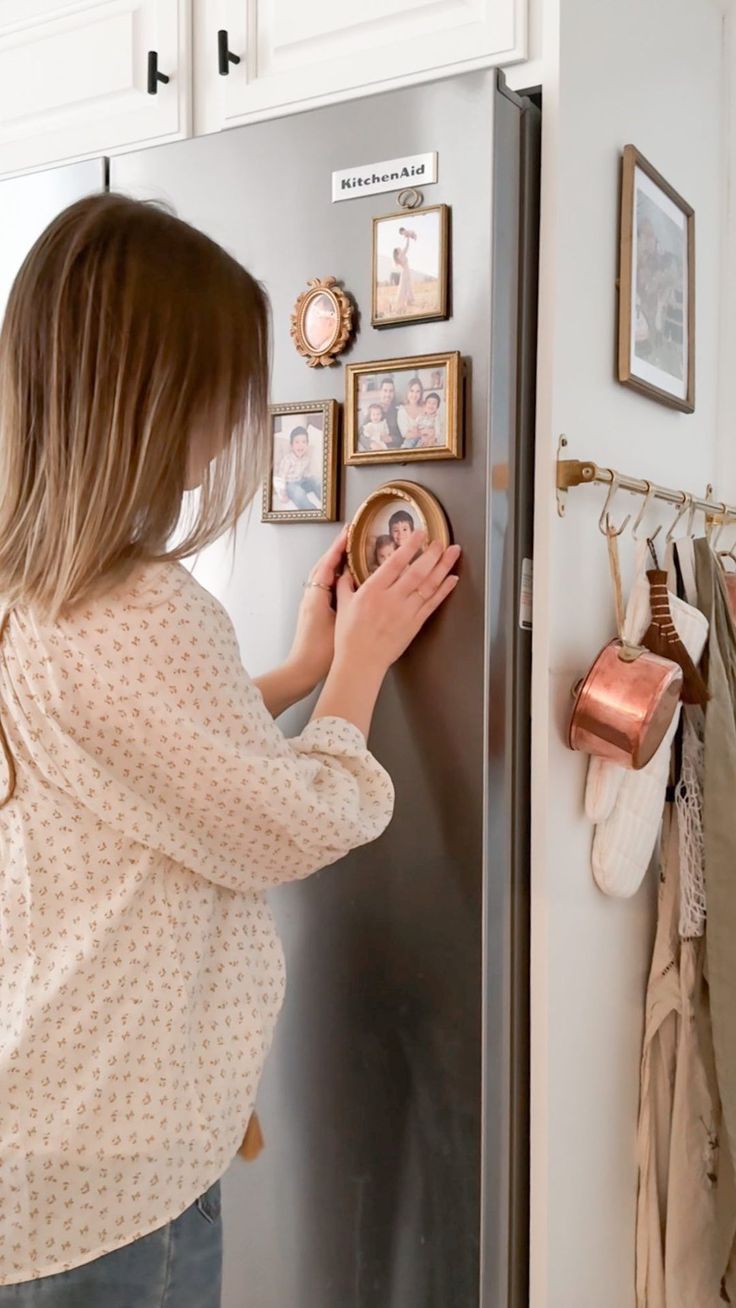 a woman is looking at pictures on the wall in front of her refrigerator and touching it with her hand