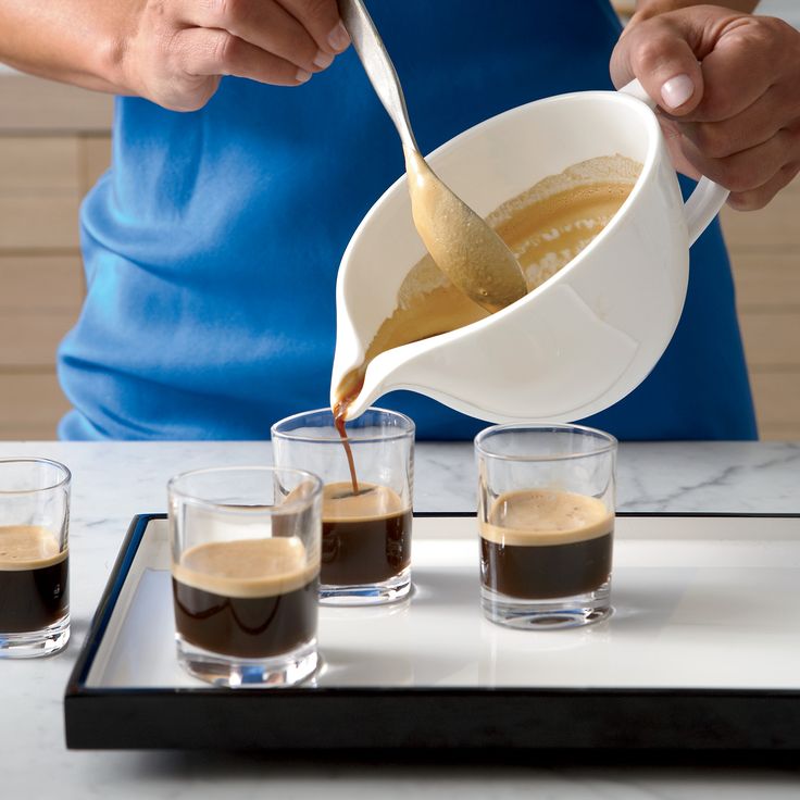 a person pouring coffee into shot glasses on a tray with three shots in front of them