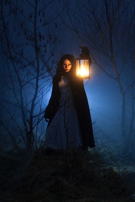 a woman holding a lantern in the woods at night