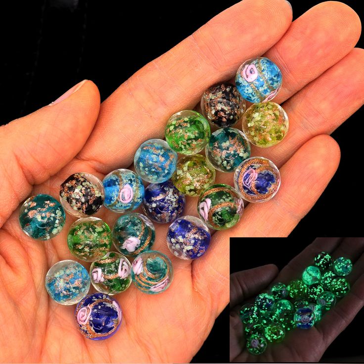 several different colored glass beads in the palm of someone's hand, one being filled with green and blue marbles