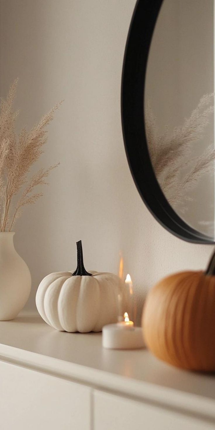 two white pumpkins sitting on top of a dresser next to a mirror and candle