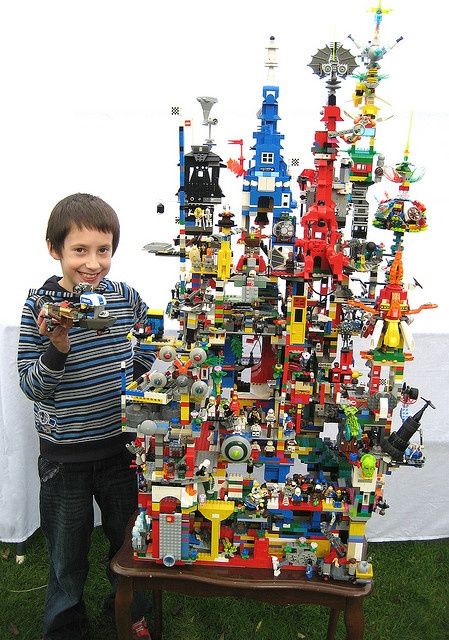 a young boy standing next to a lego christmas tree made out of many different types of toys