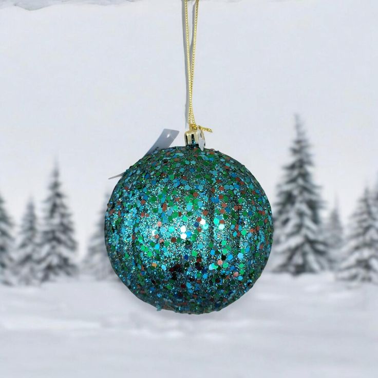 a green ornament hanging from a rope in front of snow covered pine trees