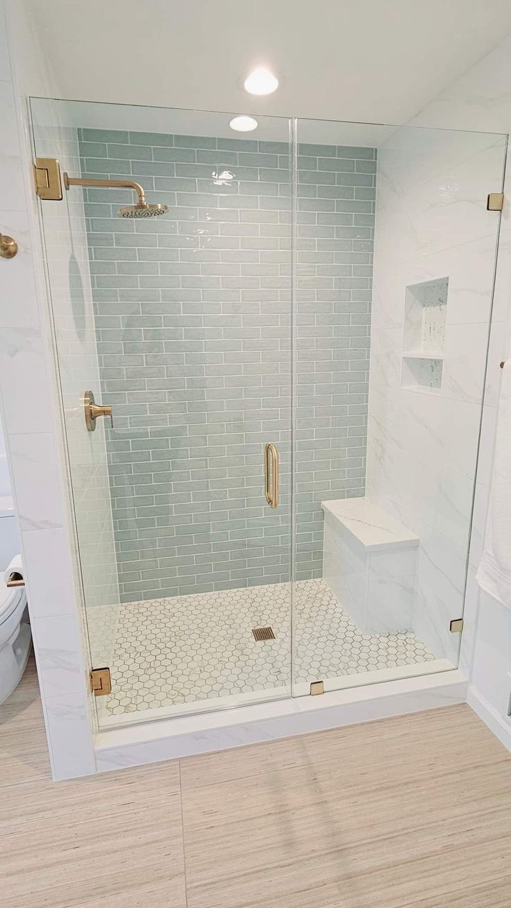 a bathroom with a walk in shower next to a white toilet and wooden flooring