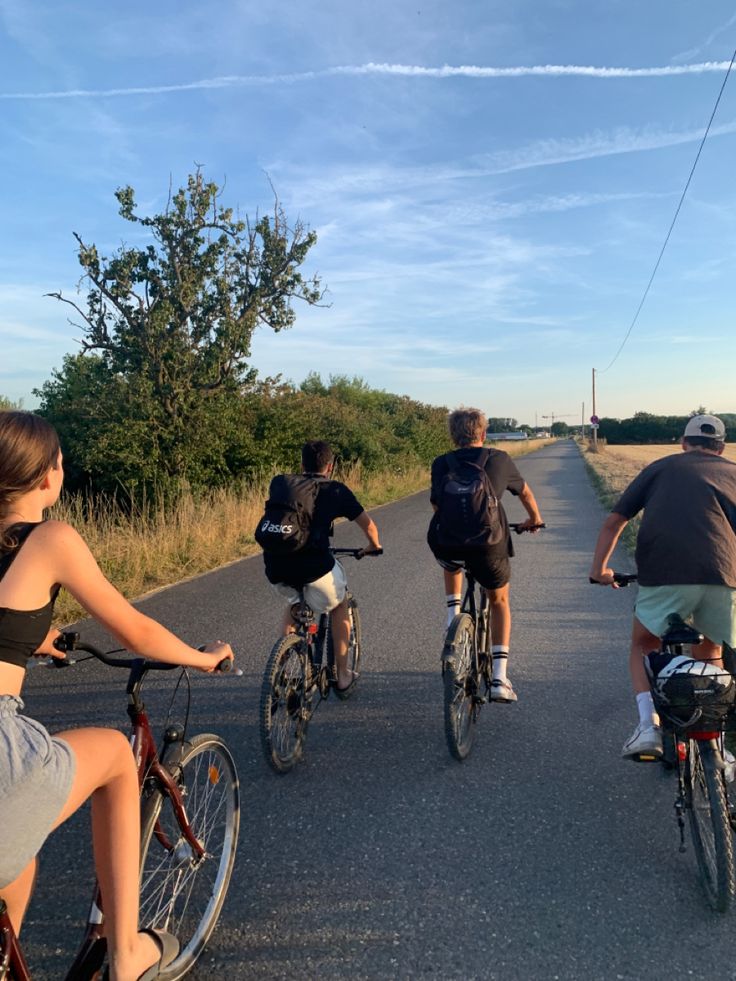 three people riding bikes down the middle of a road