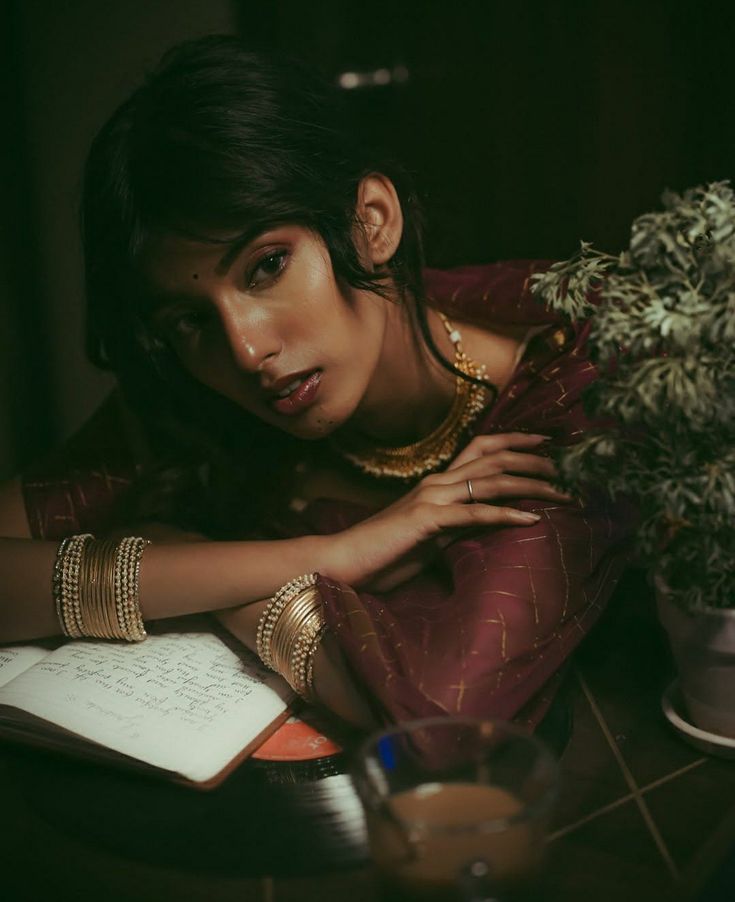 a woman sitting at a table with a book and plant in front of her face