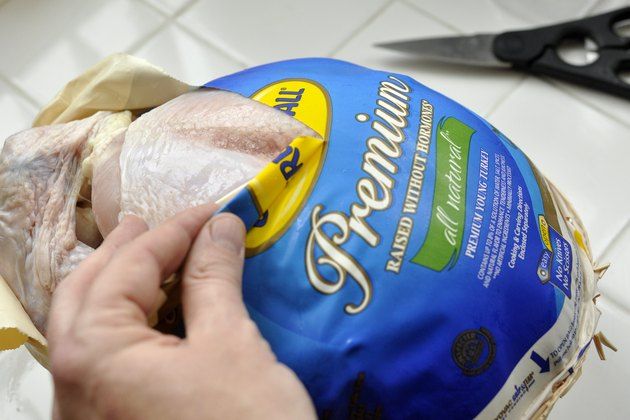 a person holding a bag of chicken on top of a counter next to a pair of scissors