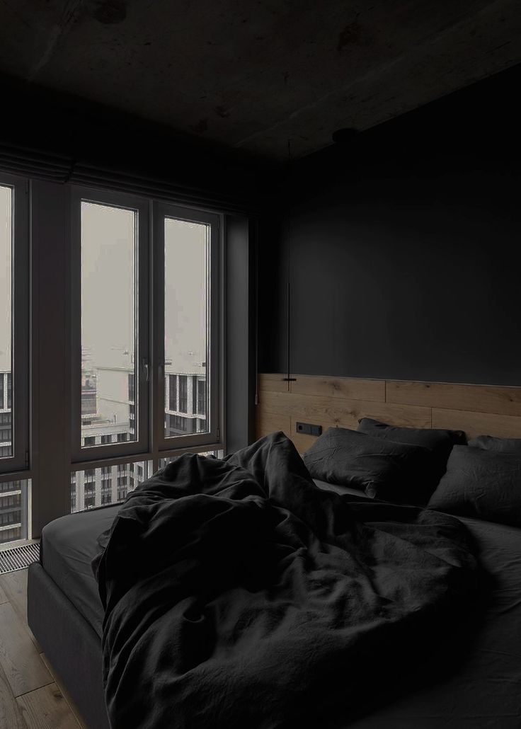 an unmade bed with black sheets and pillows in front of large windows overlooking the city