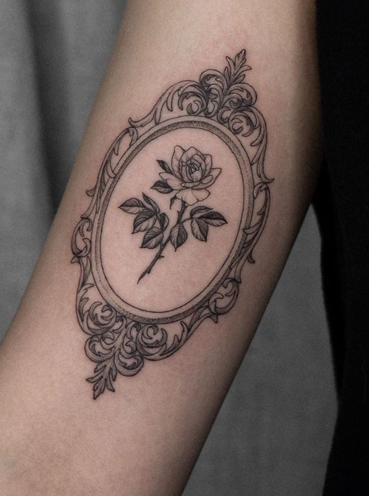 a woman's arm with a rose in a frame tattoo on the left forearm