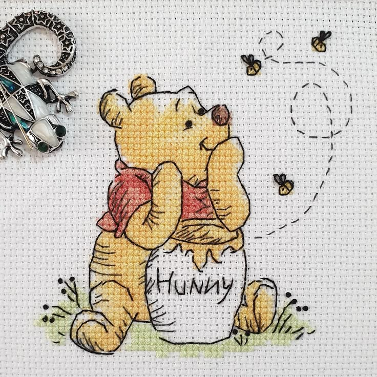 a cross - stitch picture of a teddy bear holding a honey jar with bees around it