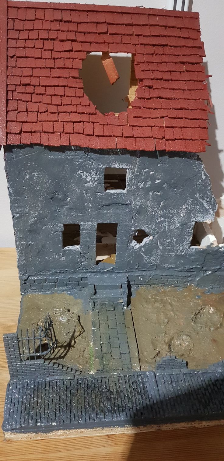 a small model of a house with a hole in the roof and a brick wall behind it