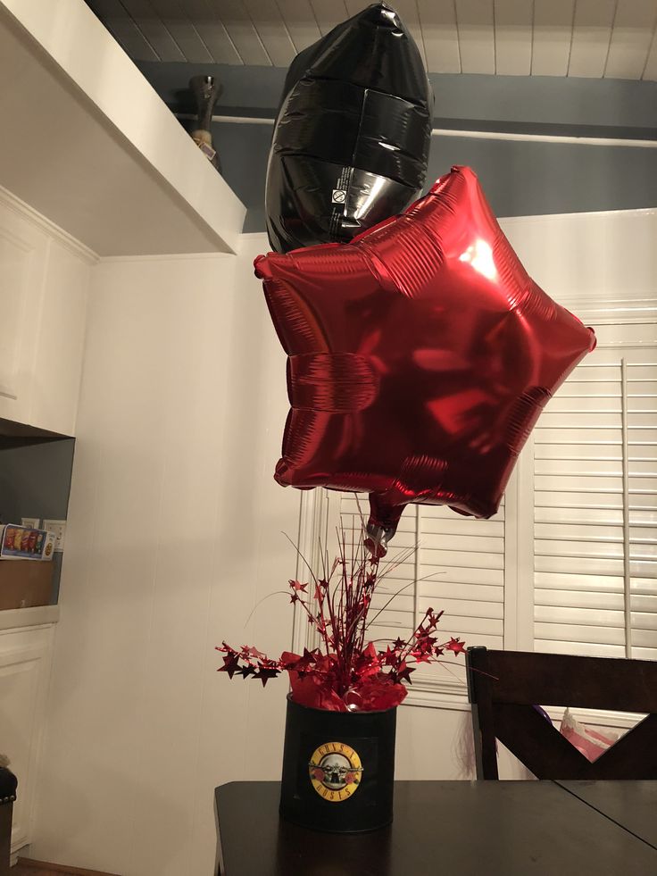 some red foil balloons are in a black vase on a table and the balloon is shaped like a star wars helmet