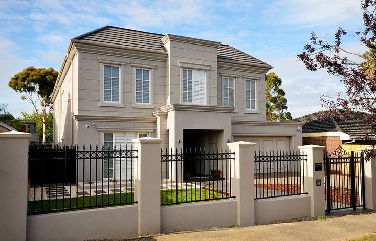 a white house with black fence and trees in the background