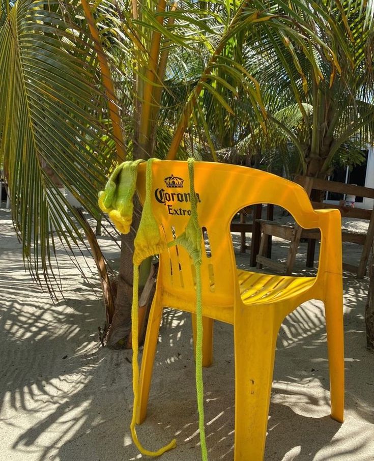 a yellow plastic chair sitting on top of a sandy beach next to palm tree leaves