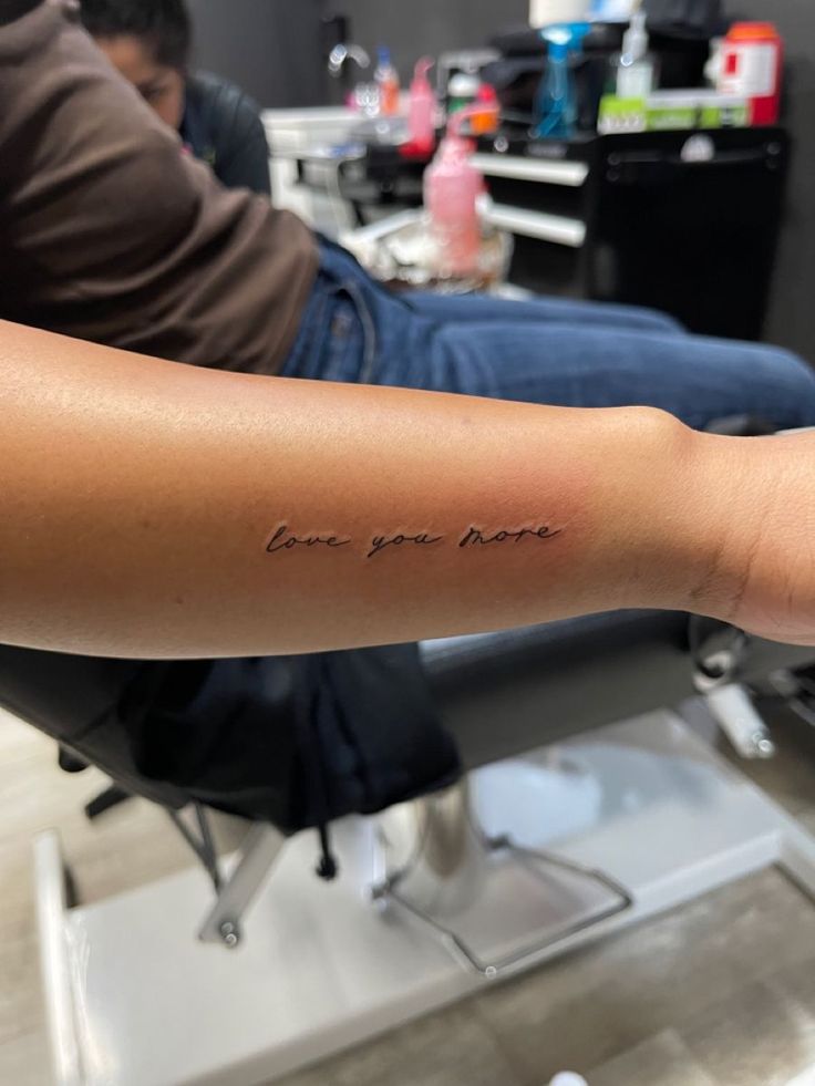 a person sitting in a chair with a tattoo on their arm that says love you mom