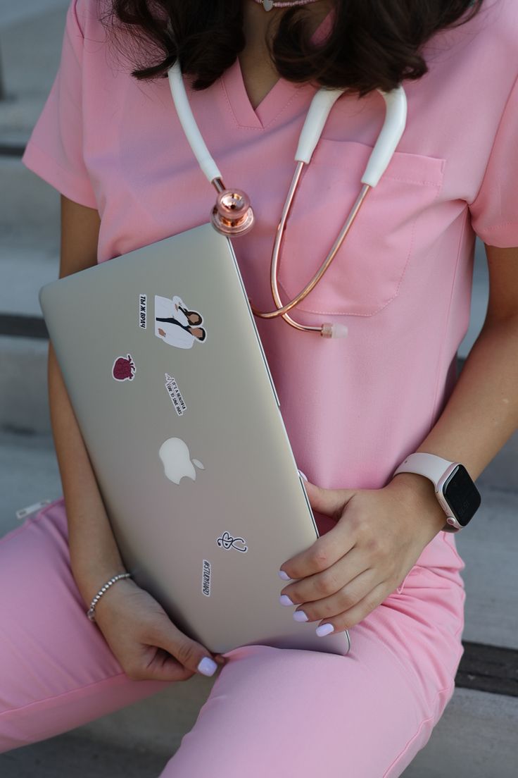 a woman in pink scrubs holding an apple laptop