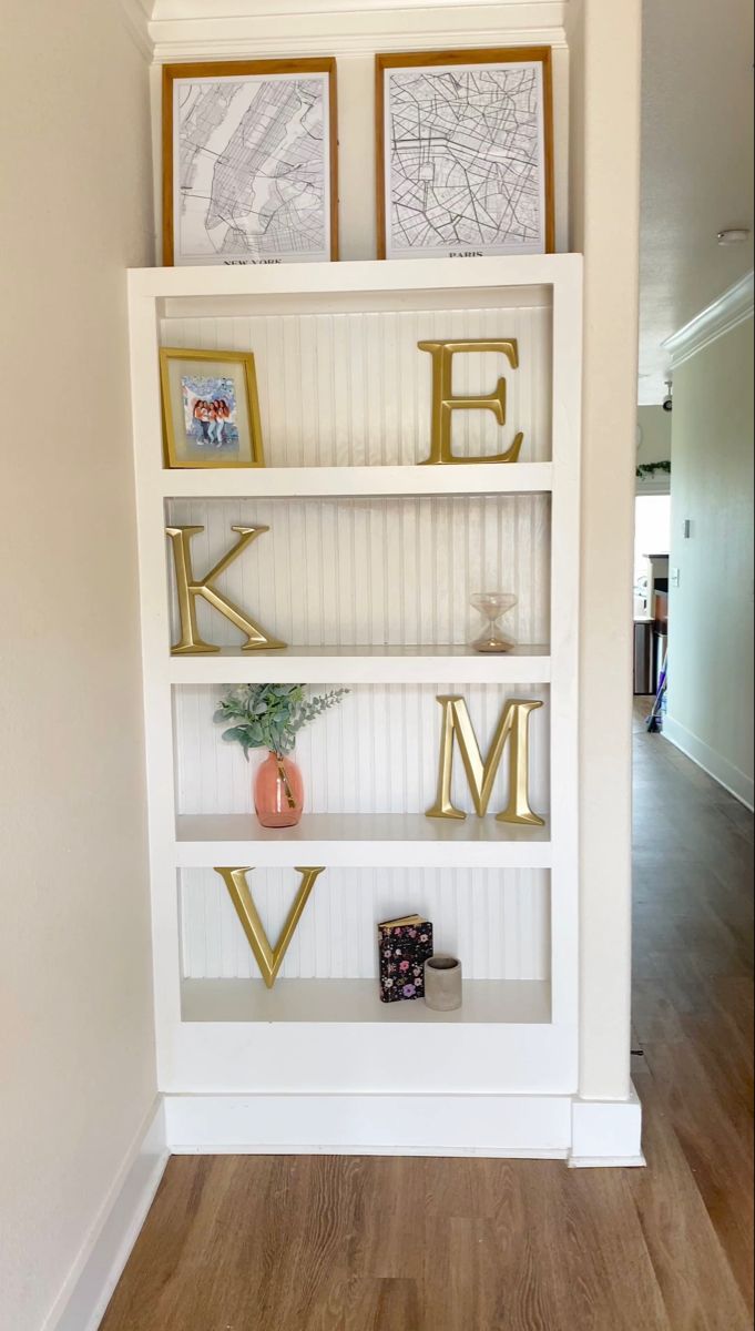 a white bookcase with gold letters and pictures on it's shelves in a home