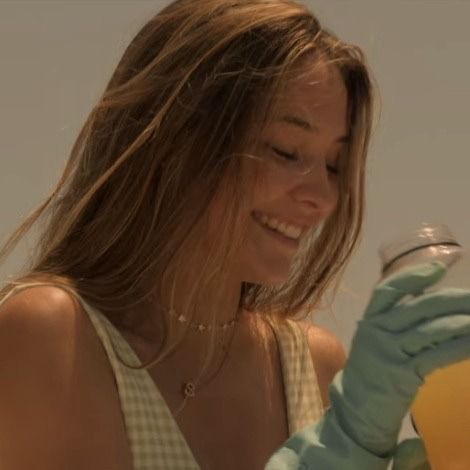 a woman in white shirt and blue gloves holding up a yellow bottle with liquid inside