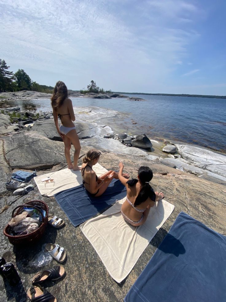 three women are sitting on the rocks by the water and one woman is doing yoga