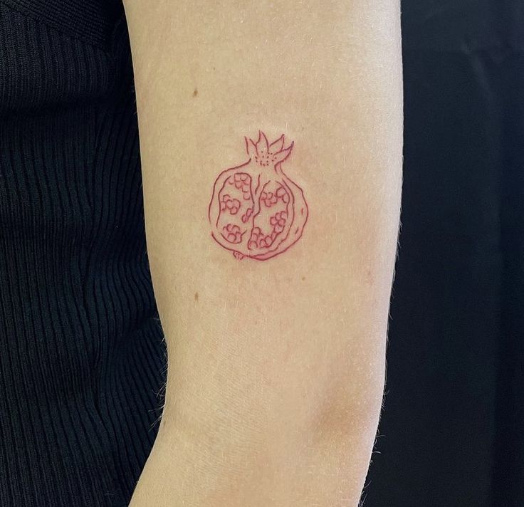 a woman's arm with a tattoo on it that has a pomegranate in the shape of a heart