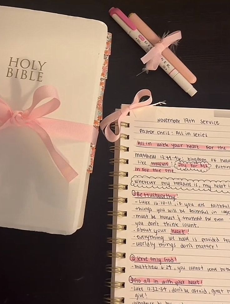 an open bible with pink ribbon and two pencils next to it