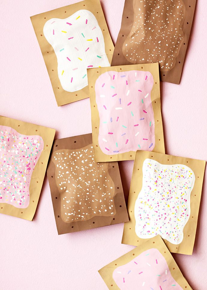 paper plates with donuts and sprinkles are on a pink surface next to brown envelopes