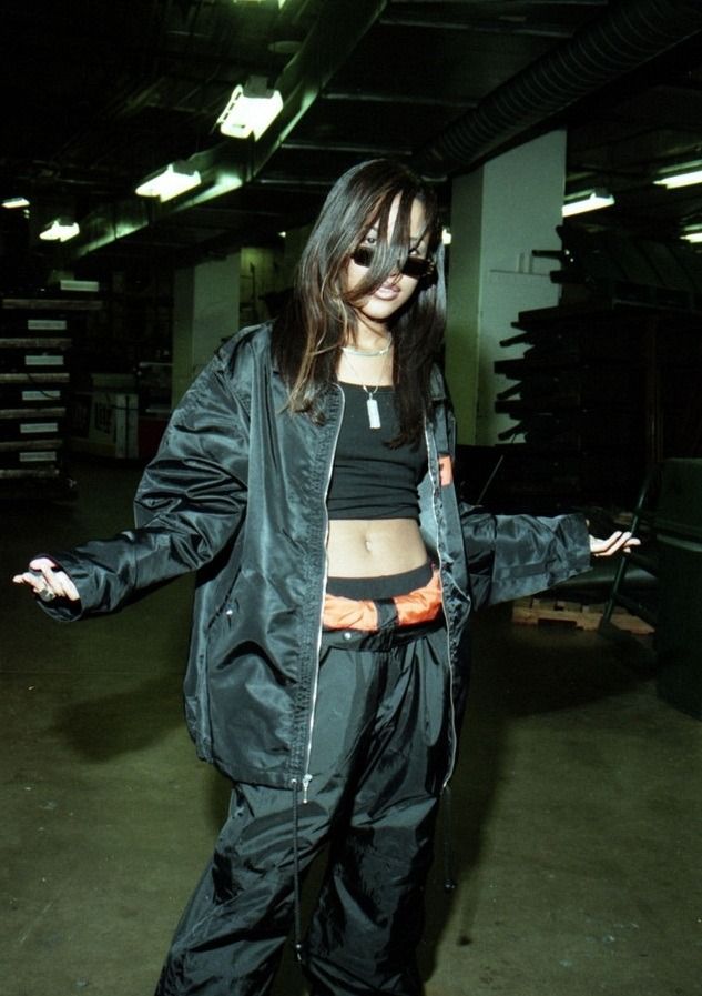 a woman standing in an empty parking garage wearing black clothing and holding her arms out