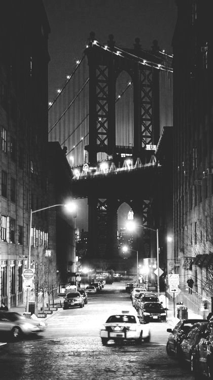 black and white photograph of cars passing under the manhattan bridge at night in new york city