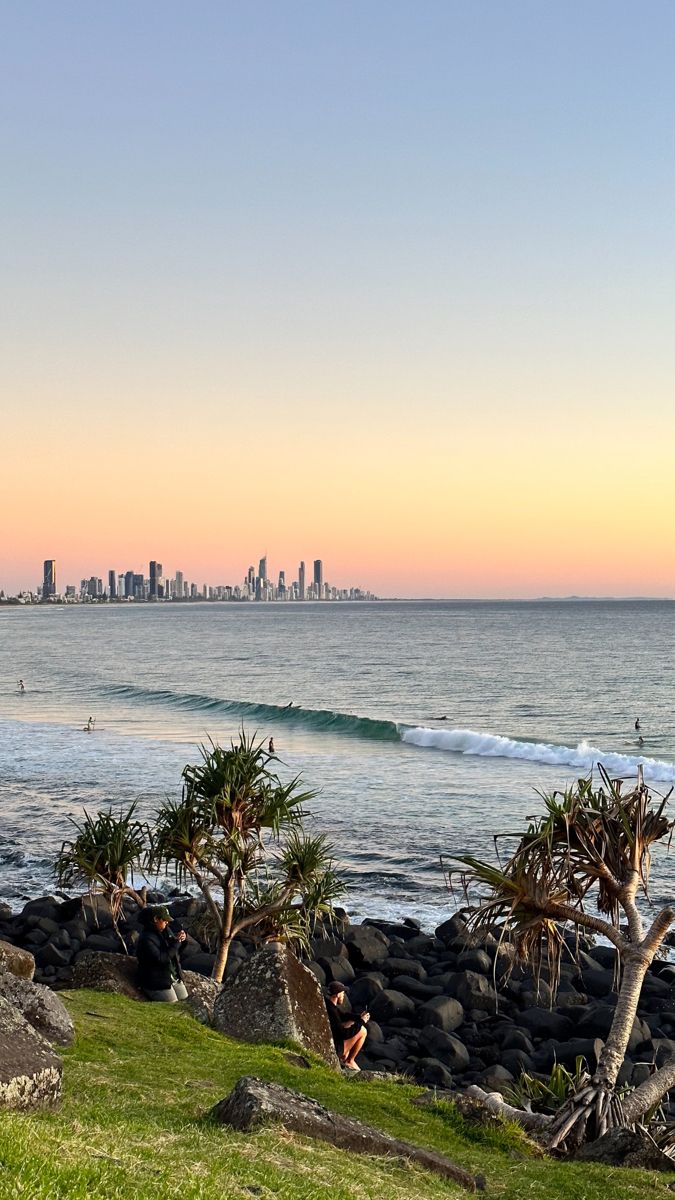 surfers ride the waves in front of an oceanfront cityscape at sunset